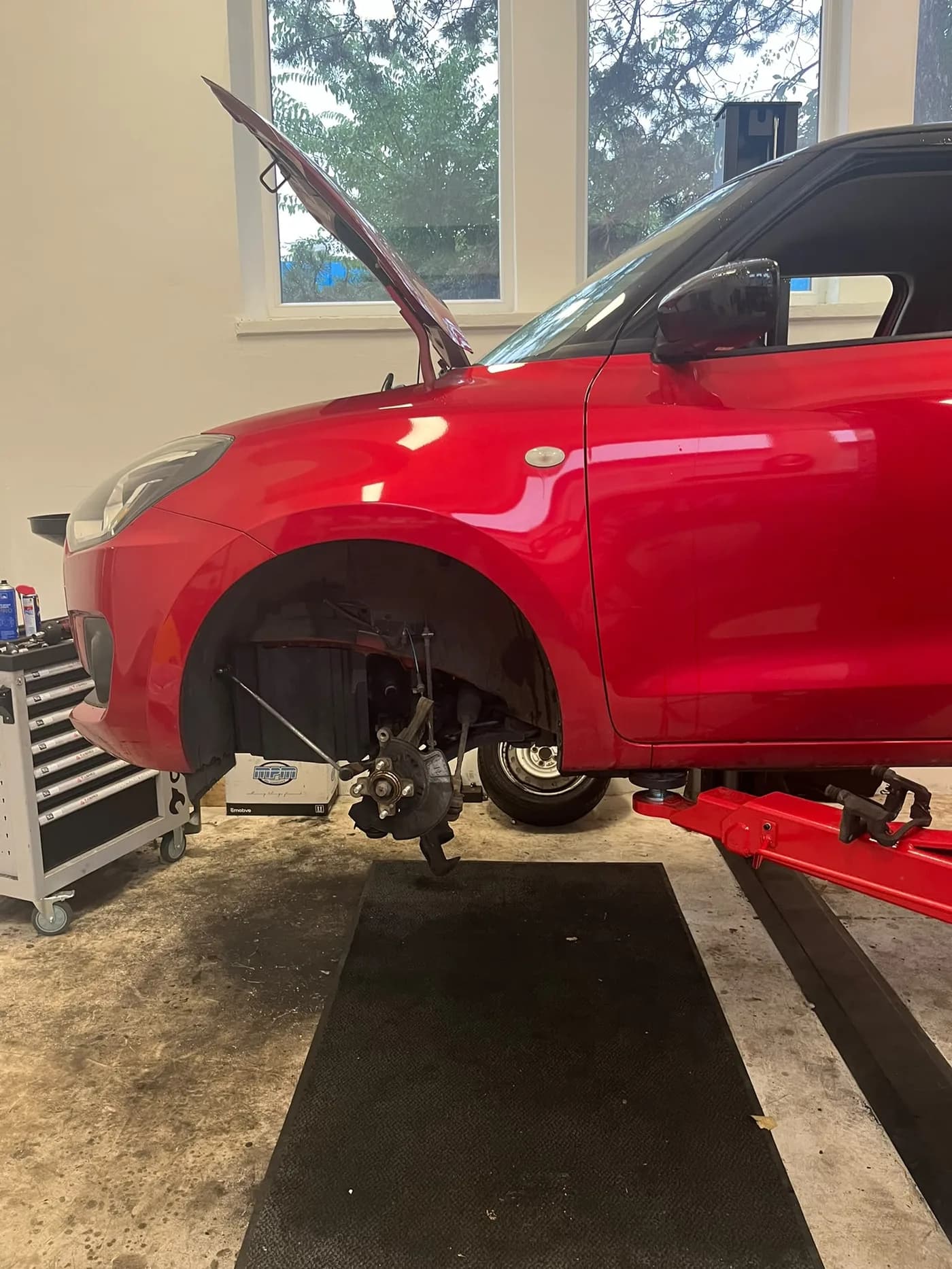 Suzuki Swift na zdviháku s demontovaným kolesom počas opravy prednej nápravy v autoservise Ludato Family, Bratislava Nové Mesto